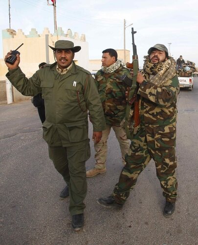 A man who identified himself as being against Libyan leader Muammar Gaddafi gestures as he holds an AK-47 rifle on the main road in Msaead