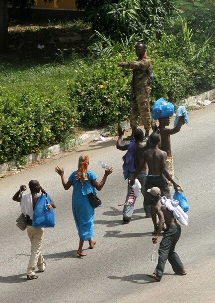 Civilians raise their hands as they walk past a pro-Gbagbo soldier in Abidjan