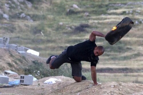 A Druze man launches a burning tire towa