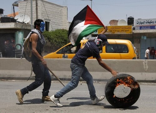 A Palestinian protester pushes a burning tyre during clashes with Israeli troops at Qalandiya checkpoint