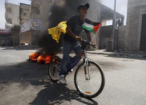 A Palestinian protester rides a bicycle during clashes with Israeli troops at Qalandiya checkpoint